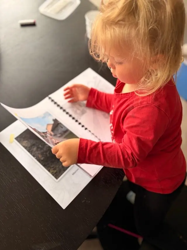 Barn flettir litabókinni þar sem hún liggur flöt á borðinu