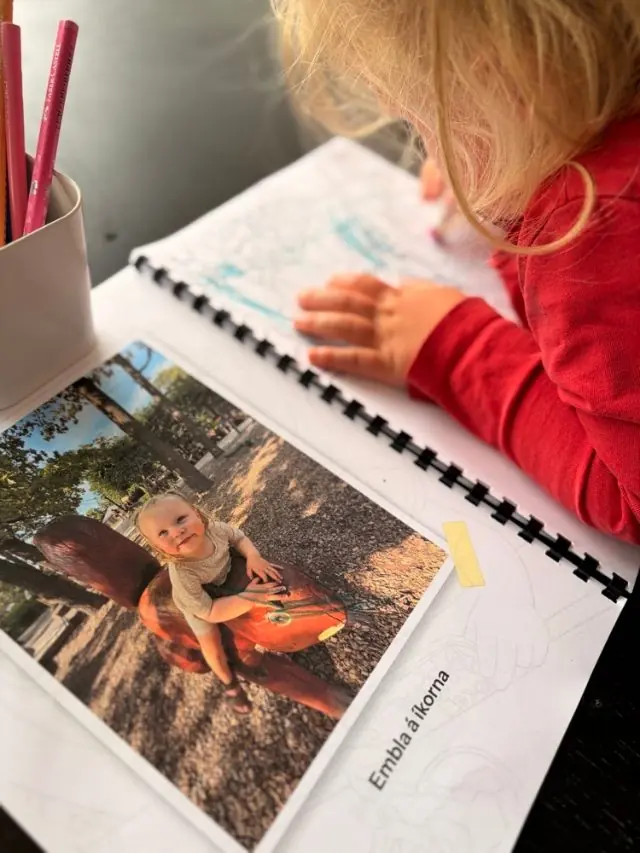 Barn litar síðu í litabókinni með bláum lit; ljósmyndin er á síðunni við hliðina
